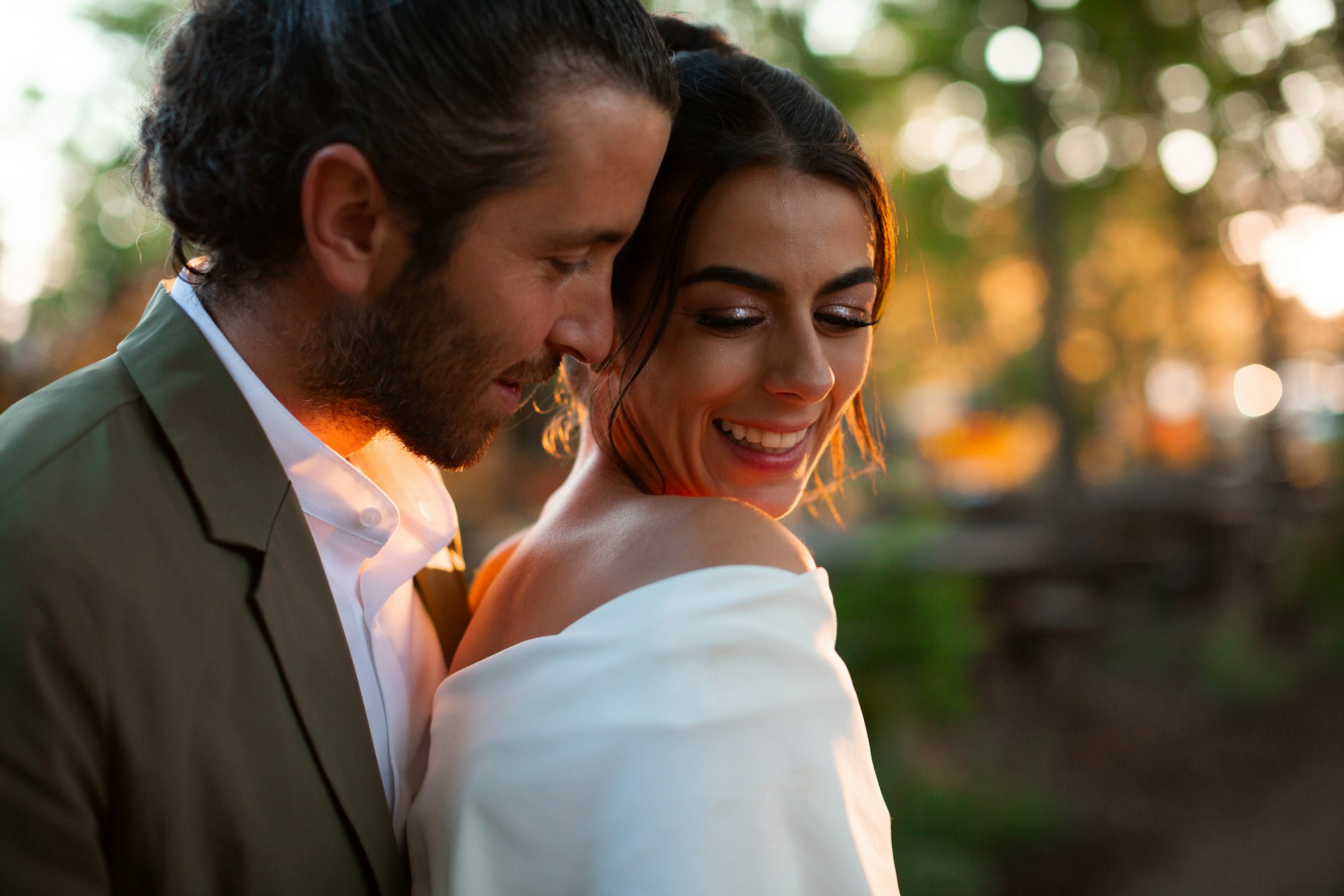 A groom holding his bride close at sunset, both smiling