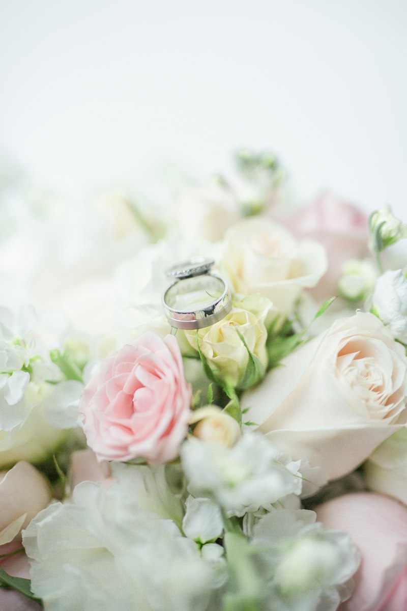 A silver wedding ring resting on a bouquet of white and pink roses
