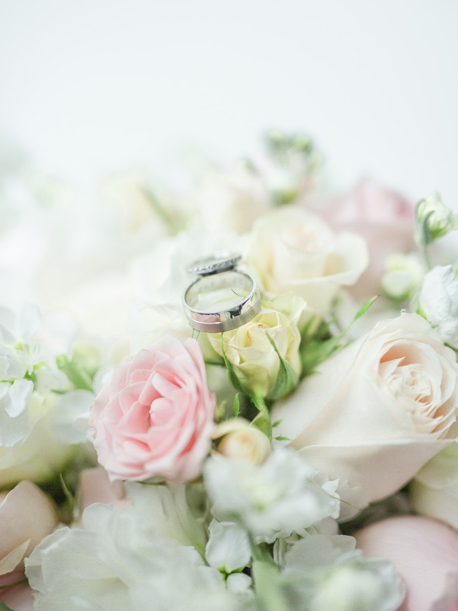 A silver wedding ring resting on a bouquet of white and pink roses