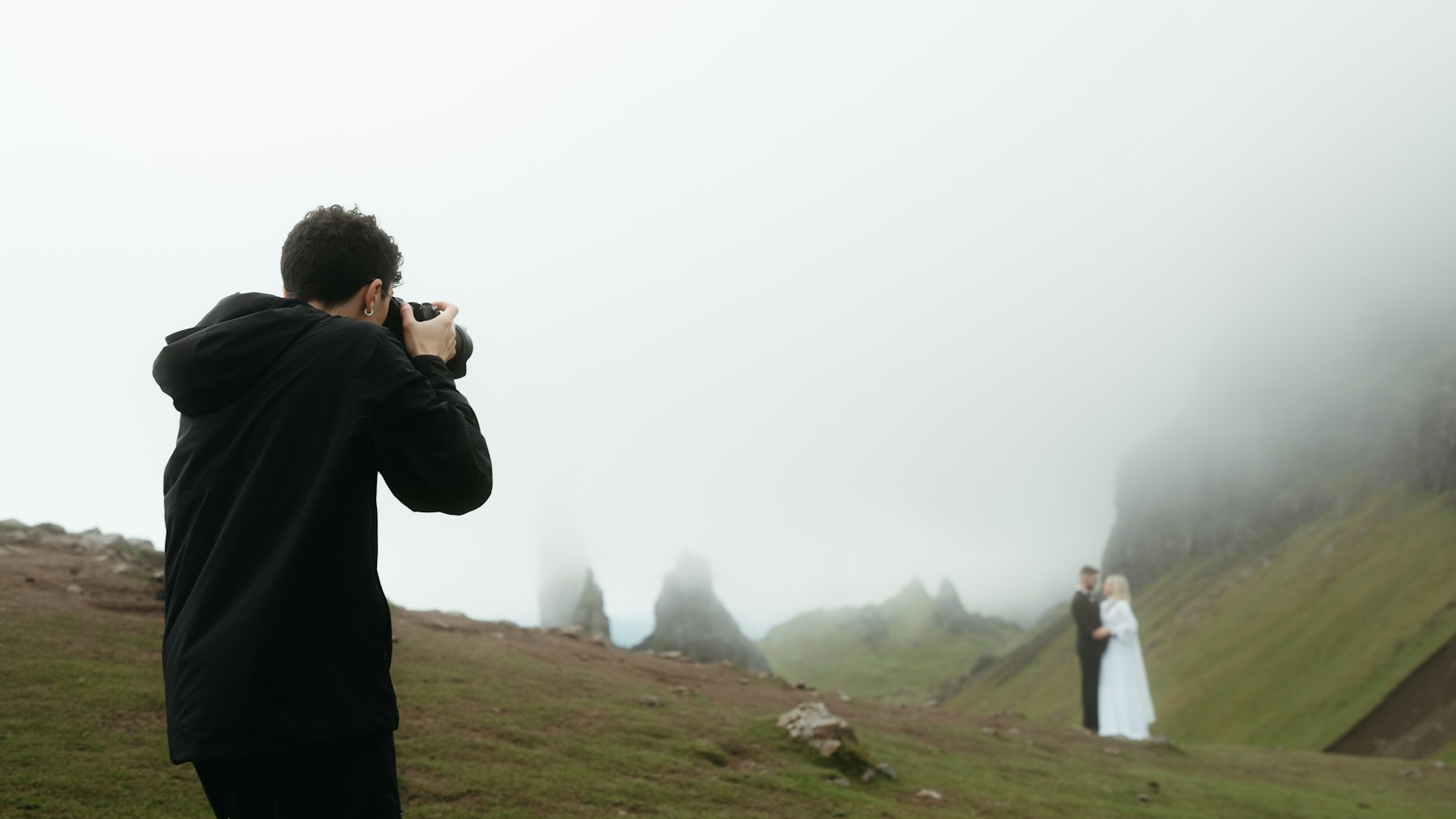 A photographer taking a picture of a couple in a foggy landscape