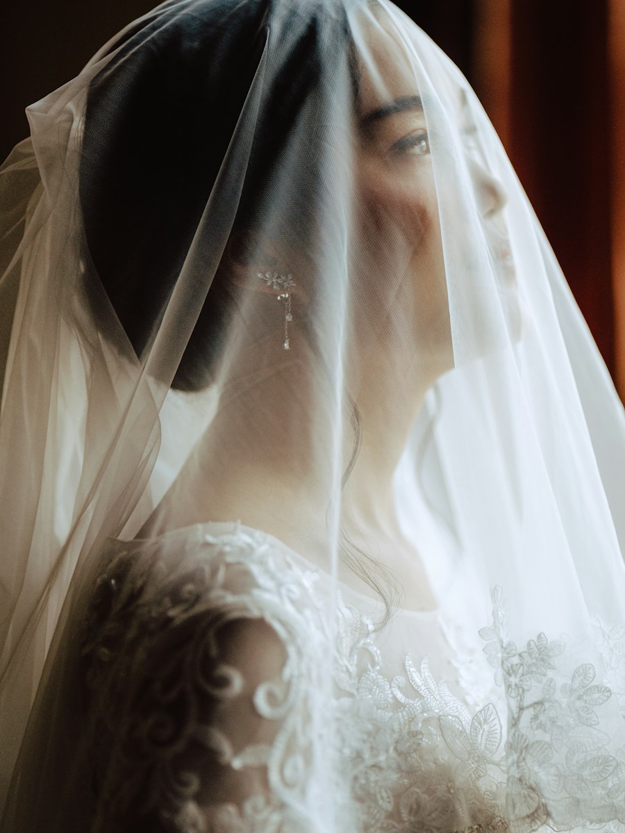 A bride in a white floral wedding gown, softly lit by natural light