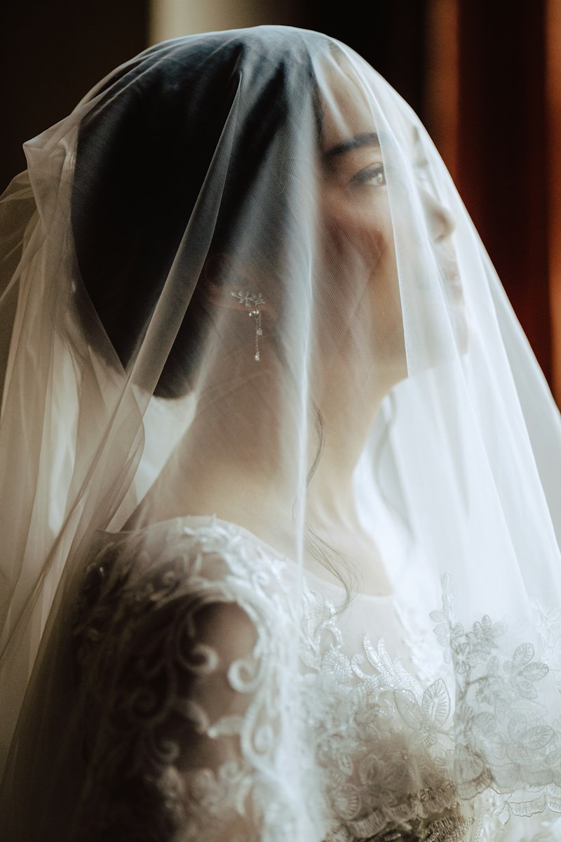 A bride in a white floral wedding gown, softly lit by natural light